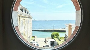 Una ventana redonda con vista a un pueblo costero, una pequeña mesa con un marco de fotos y un adorno.