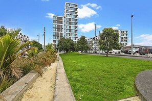 A modern building with a flat roof and multiple balconies, surrounded by a well-maintained grassy area and palm trees. - Wynyard Quarter Apartments by Urban Rest (Auckland)