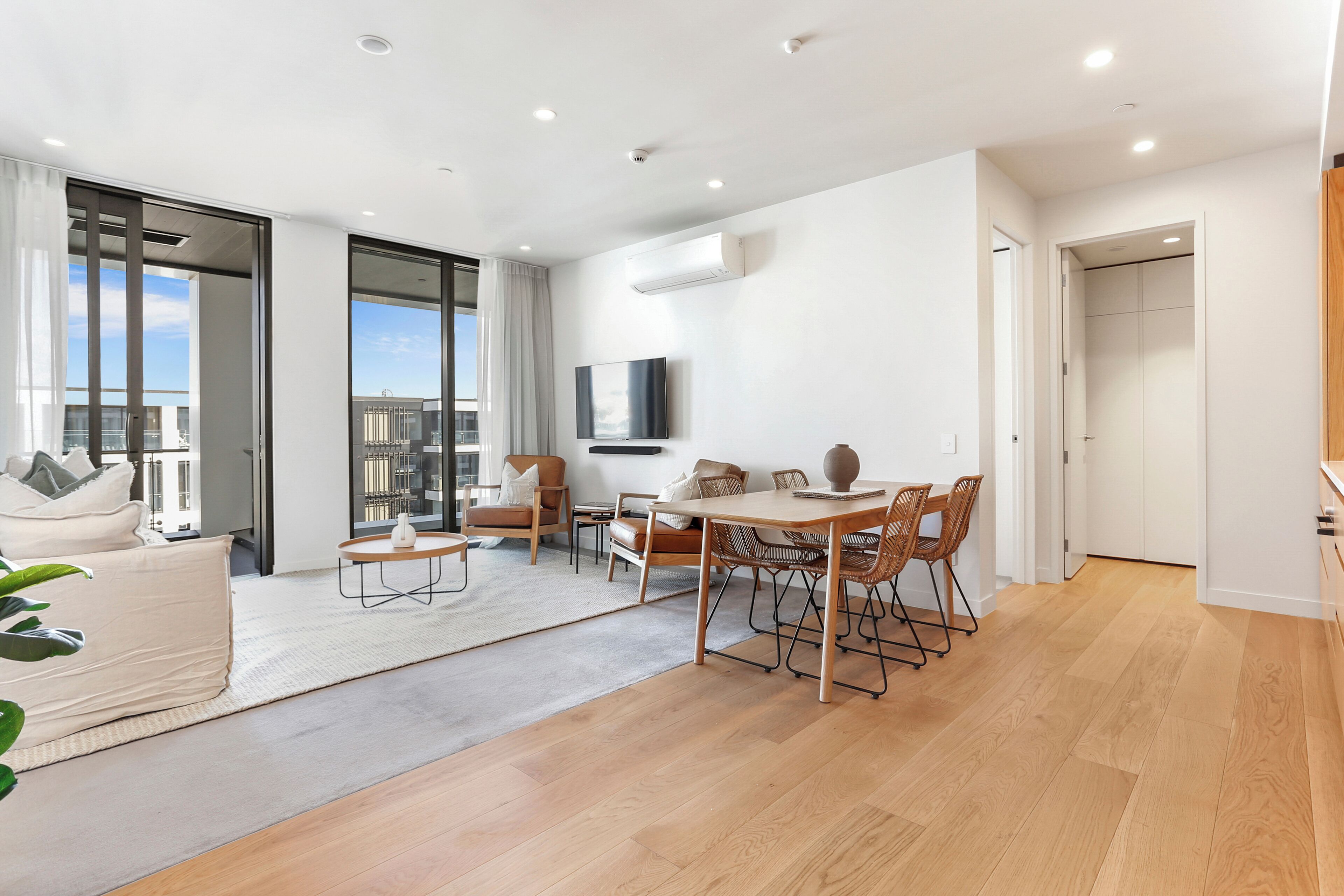 A modern living room with a dining area, large windows, and a flat-screen TV.