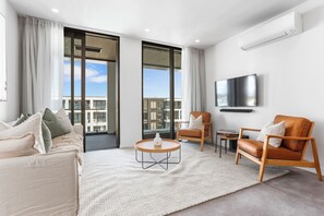 A modern living room with a sofa, two armchairs, a coffee table, and a flat-screen TV mounted on the wall. - Wynyard Quarter Apartments by Urban Rest (Auckland)