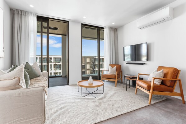 A modern living room with a sofa, two armchairs, a coffee table, and a flat-screen TV mounted on the wall. - Wynyard Quarter Apartments by Urban Rest (Auckland)