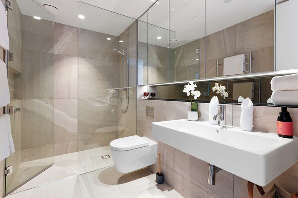 A modern bathroom with a glass shower enclosure, a white sink, and a large mirror. - Wynyard Quarter Apartments by Urban Rest (Auckland)