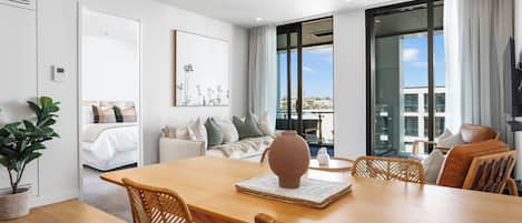 Una habitación moderna y bien iluminada con una mesa de comedor de madera, sillas de mimbre, un jarrón grande y vistas de la ciudad a través de amplias ventanas.