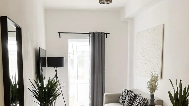 A modern living room with a sofa, a coffee table, and two potted plants. There is a large mirror on the wall and a hanging light fixture. - London Stylish 1 Bedroom Apartment With Garden (London)