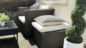 An outdoor seating area with wicker furniture, a small table, and a potted plant. - London Stylish 1 Bedroom Apartment With Garden (London)