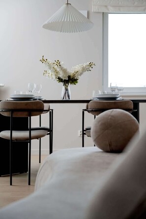 A dining area with two chairs, a table set with plates and glasses, a vase with flowers, and a hanging light fixture.