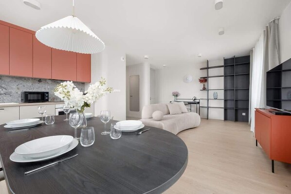Una cocina moderna con una mesa de madera oscura dispuesta para comer, un jarrón blanco con flores y una lámpara colgante blanca.