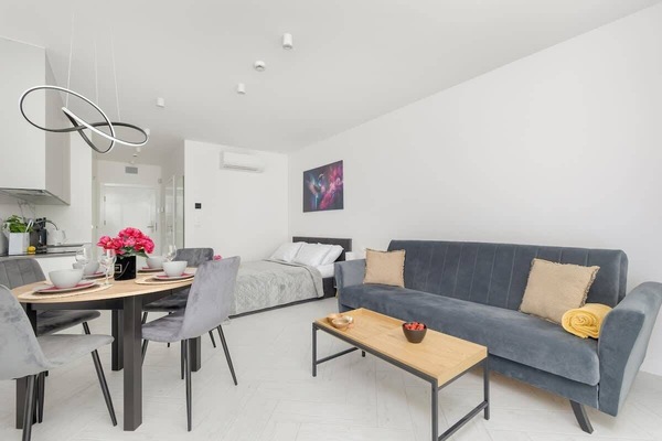 A bright living room with a sofa, dining table, and minimalist décor arranged in an open-plan layout.