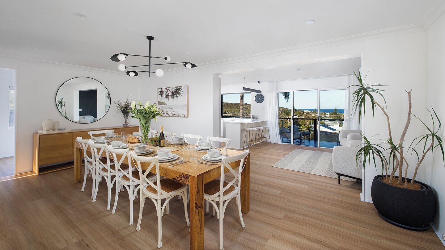 A spacious dining area with a wooden table and white chairs, a large mirror, and a view of the outdoors.