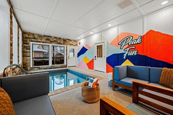 A pool area with a stone wall, a colorful mural, and a seating area with a couch and a wooden bench. - Cabin near Wax Museum w/indoor pool & hot tub (Pigeon Forge)