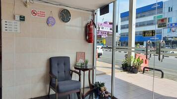 A reception area with a chair, a clock, a fire extinguisher, and a view of the street outside.