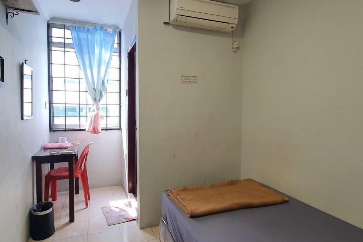 Una habitación pequeña y sencilla con cama, escritorio y silla, y ventana con cortinas.