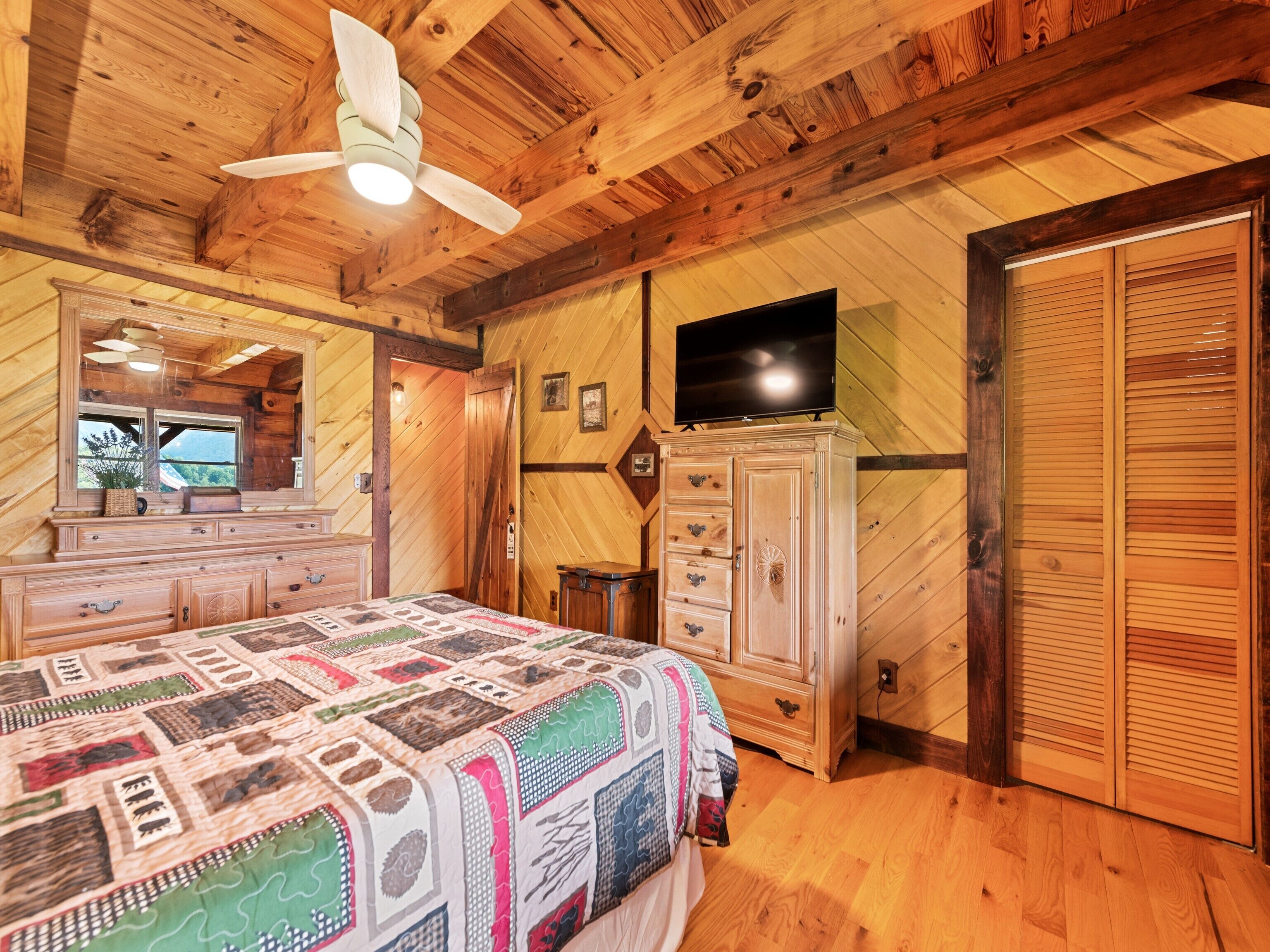 Une chambre dans une cabane en bois, avec un lit, une commode, une télévision et un ventilateur de plafond.