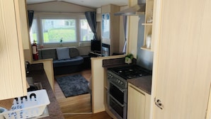 A compact kitchenette with a stove, oven, and a small countertop. There is a sofa and a window with curtains in the background.