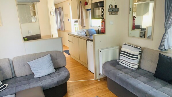 A compact living space with two grey sofas, a kitchen area with a refrigerator, and a small dining table. - Wl56 Haven Haggerston Castle Holiday Park (Berwick-upon-Tweed)