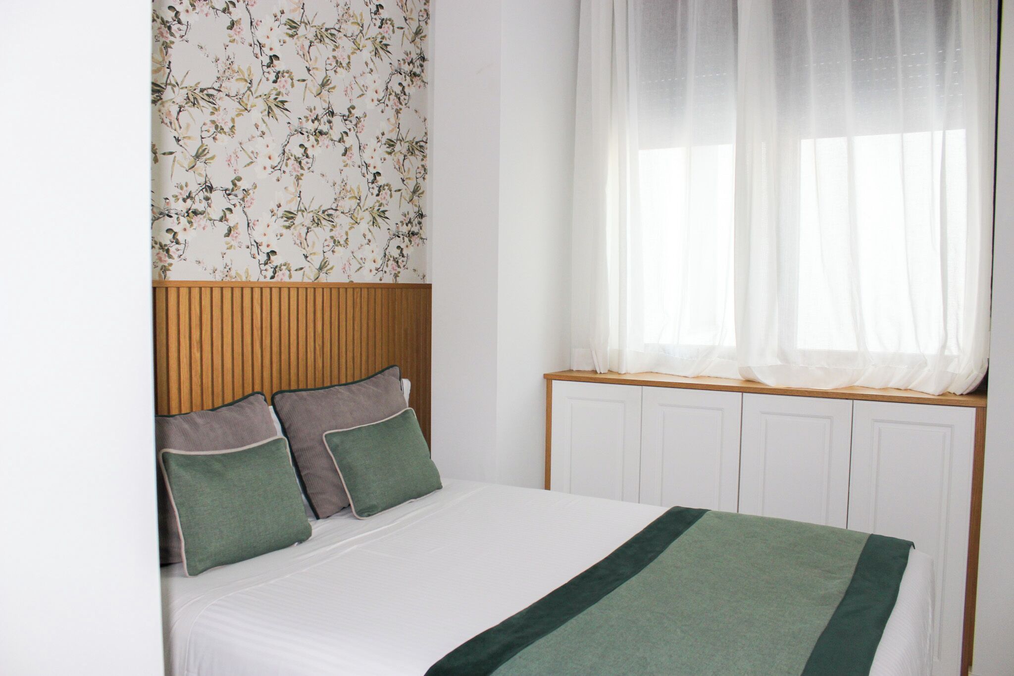 Una cama bien hecha con un plaid verde, un cabecero de madera y un estampado floral en el papel tapiz.