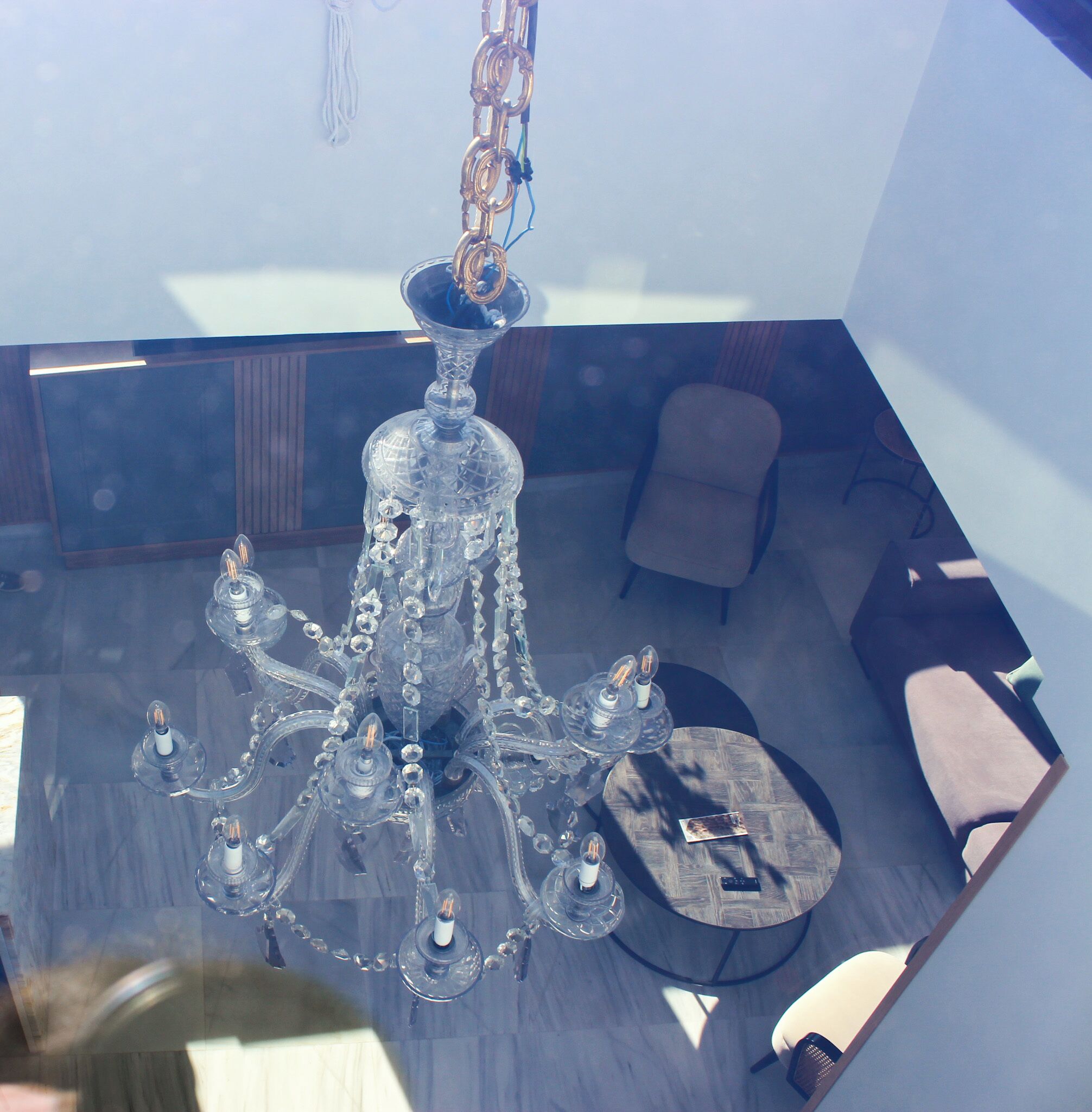 A modern interior with a crystal chandelier, a round wooden table, and a sofa.