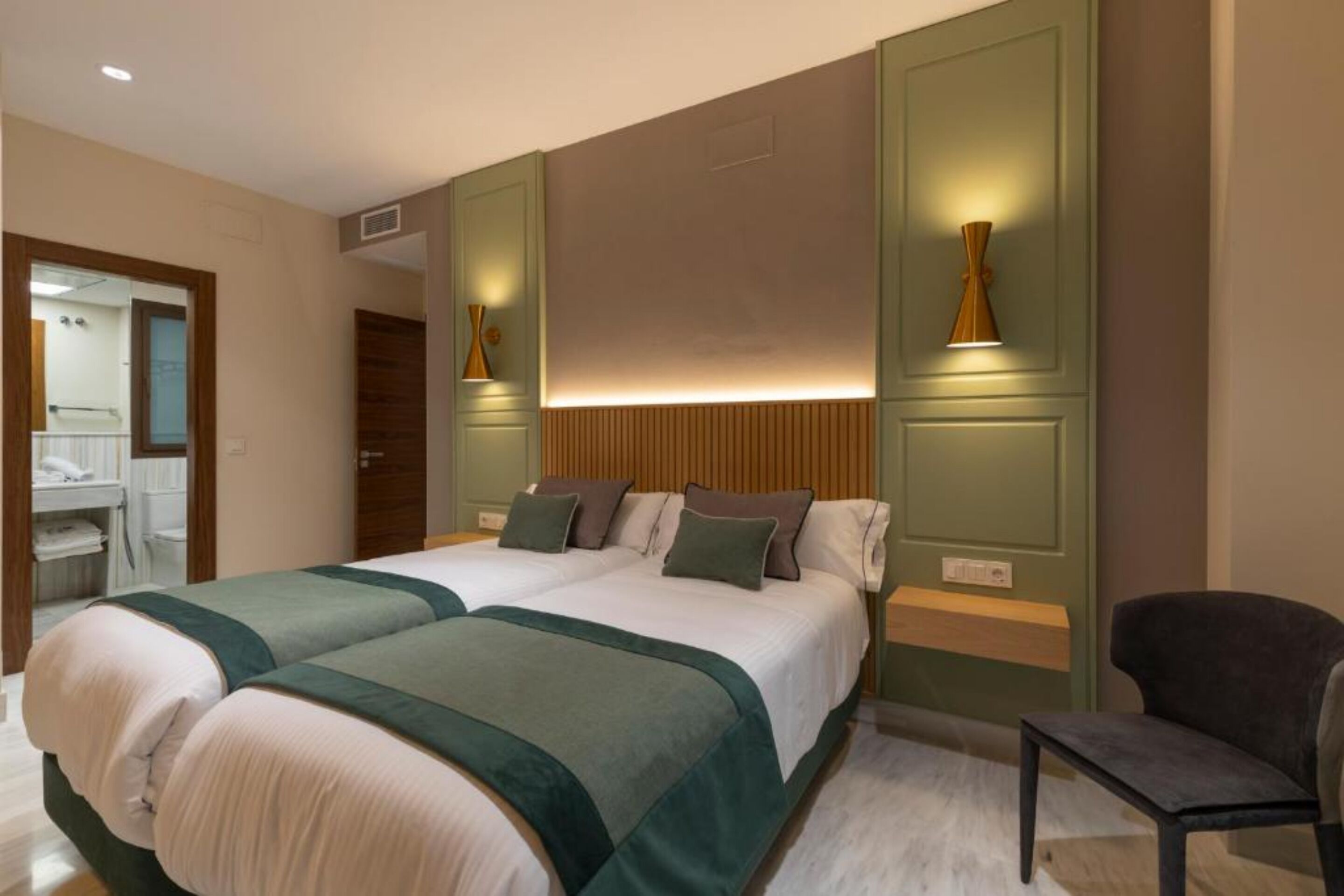 A hotel room with two beds, a chair, and a mirror.