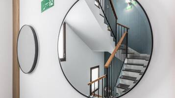 Espejo circular que refleja una escalera con barandilla de madera y pasamanos negros.