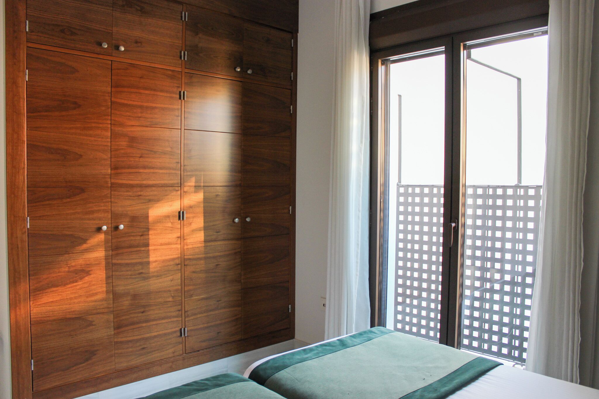 Une chambre à coucher avec une grande armoire, un lit avec une literie verte et une vue sur un immeuble par la fenêtre.