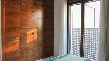 Une chambre à coucher avec une grande armoire, un lit avec une literie verte et une vue sur un immeuble par la fenêtre.