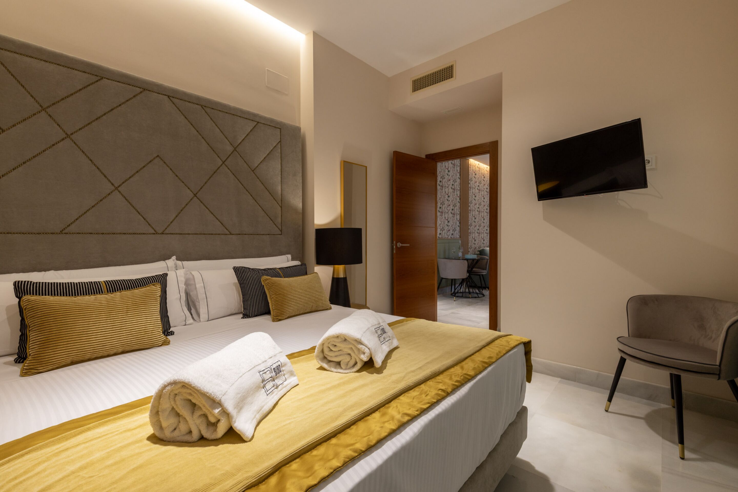 A hotel room with a large bed, a flat-screen TV mounted on the wall, and a chair.