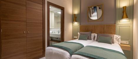A hotel room with a large wardrobe, a bed with green bedding, a mirror on the wall, and two bedside lamps.