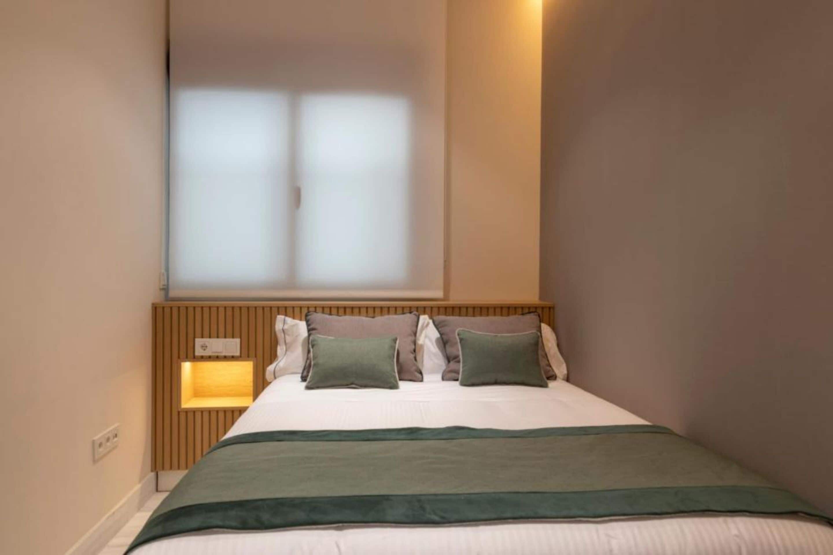 A neatly made bed with a wooden headboard, a bedside lamp, and a window with frosted glass.