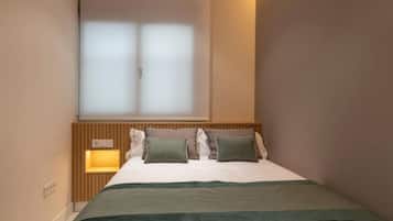 A neatly made bed with a wooden headboard, a bedside lamp, and a window with frosted glass.