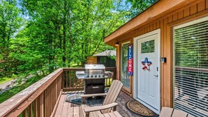 A wooden deck with a grill, outdoor seating, and a door with a 'WELCOME' sign.