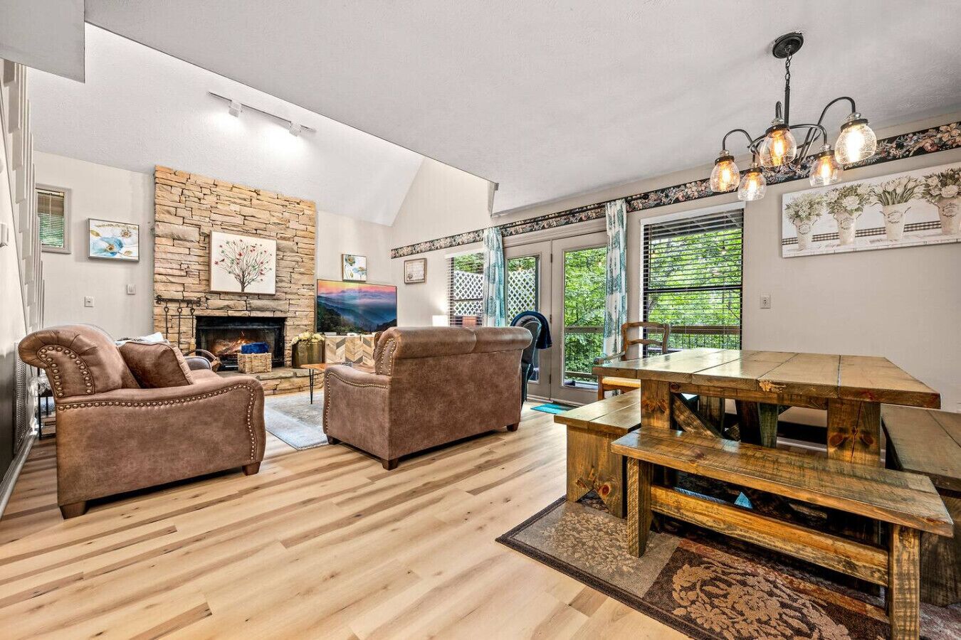 A spacious living room with a stone fireplace, wooden flooring, and a dining area with a rustic wooden table and benches.