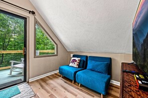 Una habitación acogedora con un sofá azul, un ventanal grande y vistas al exterior con vegetación.