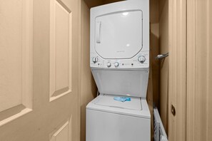 A compact laundry room with a front-loading washer and dryer, a door with a handle, and a small towel dispenser.