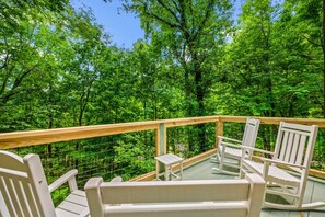Eine Holzterrasse mit weißen Schaukelstühlen und einem kleinen Tisch, umgeben von üppigen, grünen Bäumen.
