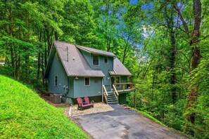 A two-story cabin with a front porch, a small deck, and a driveway.