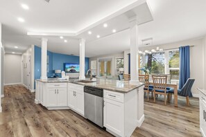 A modern kitchen with white cabinetry, a built-in dishwasher, and a dining area with wooden chairs and a table.