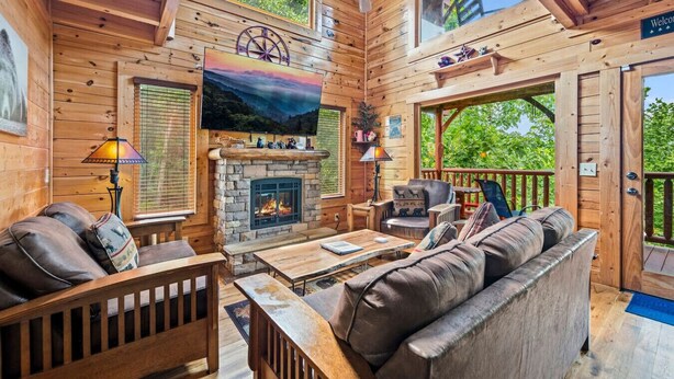 Un interior de cabaña acogedor con chimenea, muebles de madera y una vista panorámica por las ventanas.
