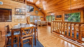 Interior de una cabaña de troncos con comedor, sofá y balcón con barandilla de madera.