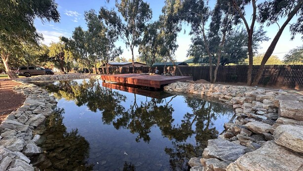 A pond with a wooden deck and stone border, surrounded by trees and a fence. - Cozy Desert Villa Sleeps 5, Heated Pool | Solana 4 (Tucson)
