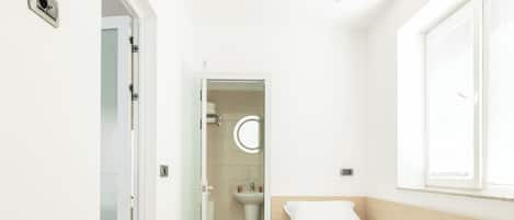 Ein Hotelzimmer mit Holzboden, zwei Betten, einem Fenster und einem Badezimmer mit Waschbecken und Toilette.