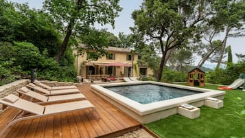Un jardin avec une piscine, des chaises longues, une terrasse en bois et une petite maison de jeu.