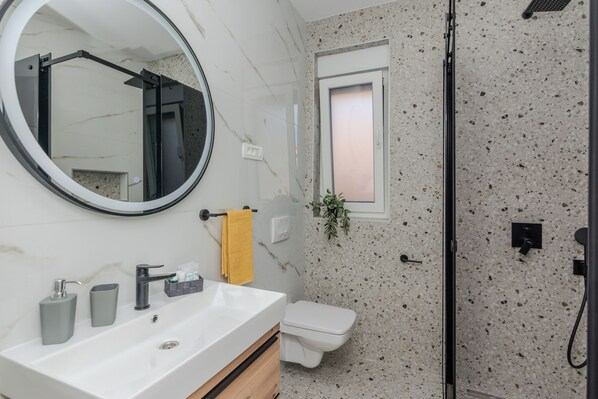 A bathroom with a white sink, a mirror, a toilet, and a shower area. - Apartments Fil Cosic (Vir)