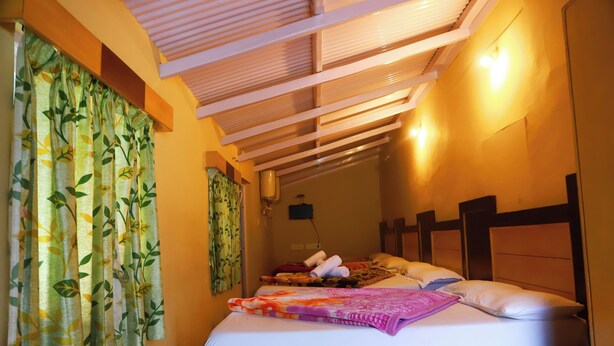 A hotel room with a bed, a headboard, a nightstand, and a ceiling with wooden beams. - SSG COTTAGE (Ootacamund)
