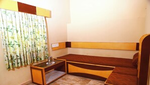 A small room with a bed, a nightstand, and a window with curtains. - SSG COTTAGE (Ootacamund)