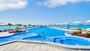 A swimming pool with lounge chairs and umbrellas, surrounded by a clear blue sky and ocean view. - Address  Beach Resort Marassi (El Alamein)