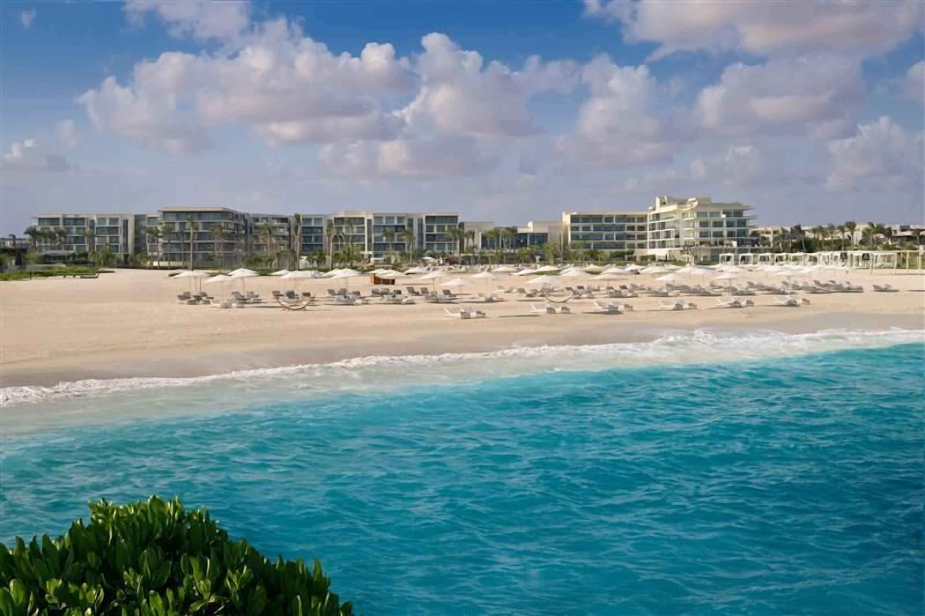 A beachfront hotel with multiple buildings, a sandy beach, and lounge chairs.