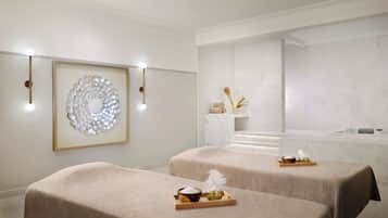 Relax in a serene spa room with two treatment tables, a marble wall, and a bathtub.