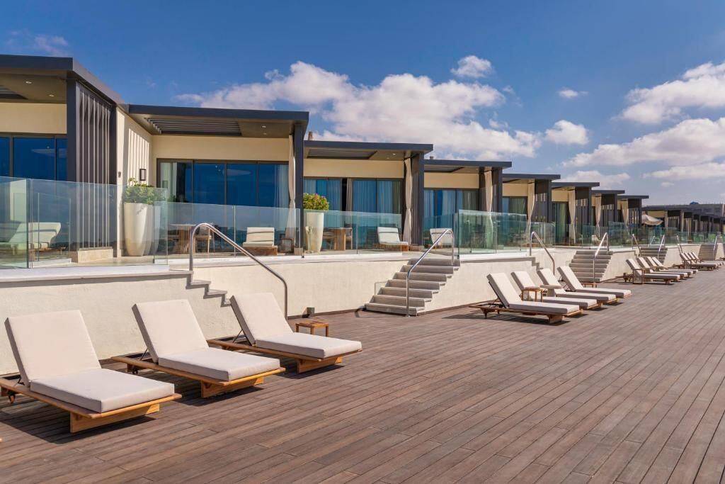 A modern resort with a wooden deck, multiple lounge chairs, and a clear sky.