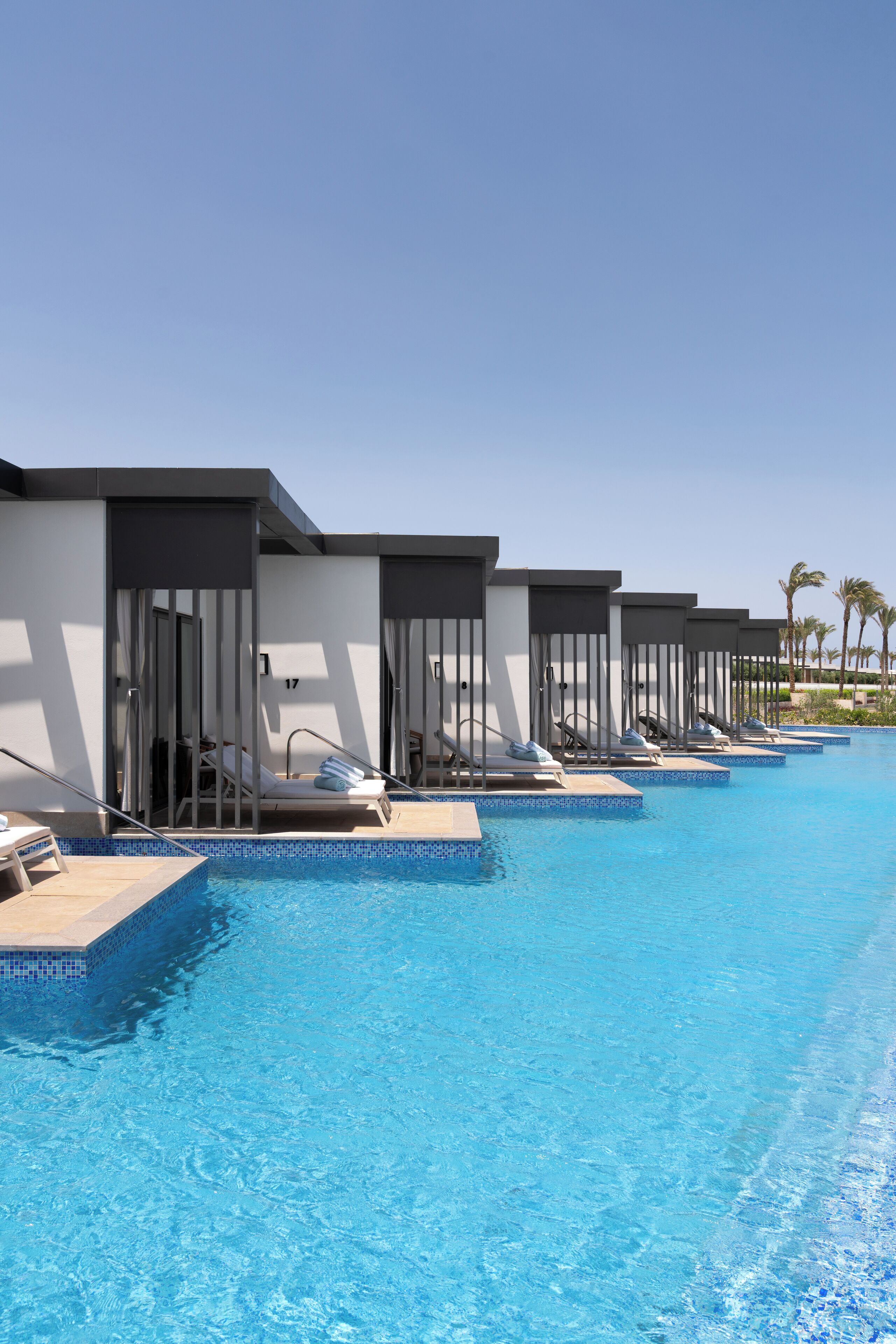 A poolside area with multiple lounge chairs and overwater bungalows.