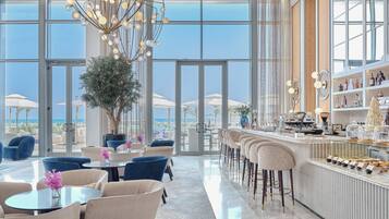 A modern bar area with a long counter, bar stools, and a view of the beach through large windows.